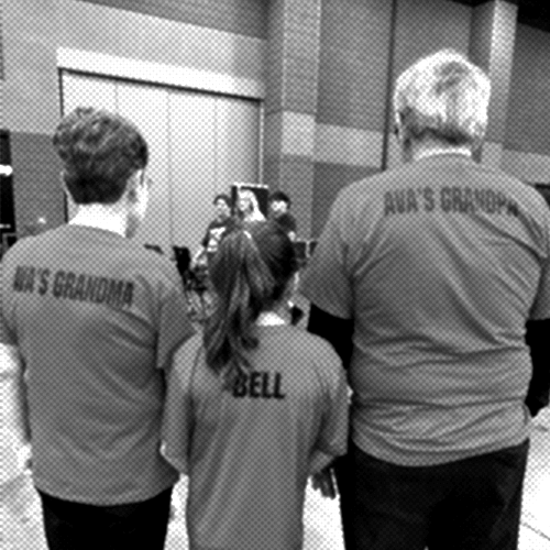 Ava in a red shirt riding an escalator, carrying a large, teal, sticker-covered plastic bow case. She is looking back over her shoulder.